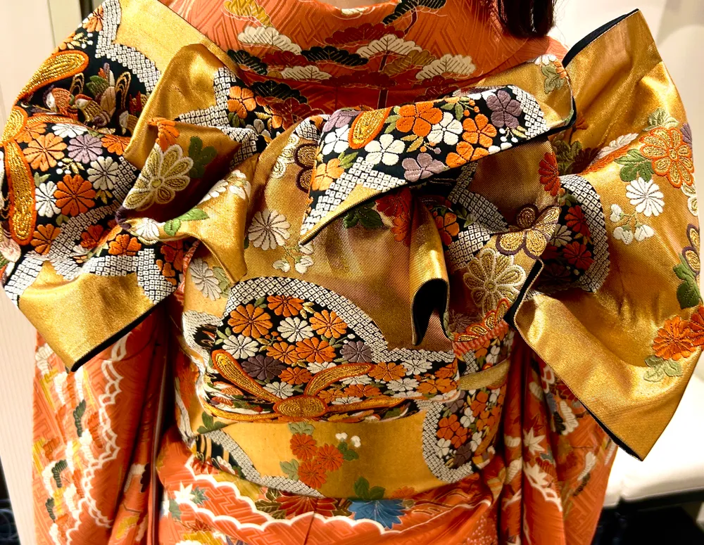Close-up of an orange and gold obi with elaborate floral embroidery, worn over a coral kimono.