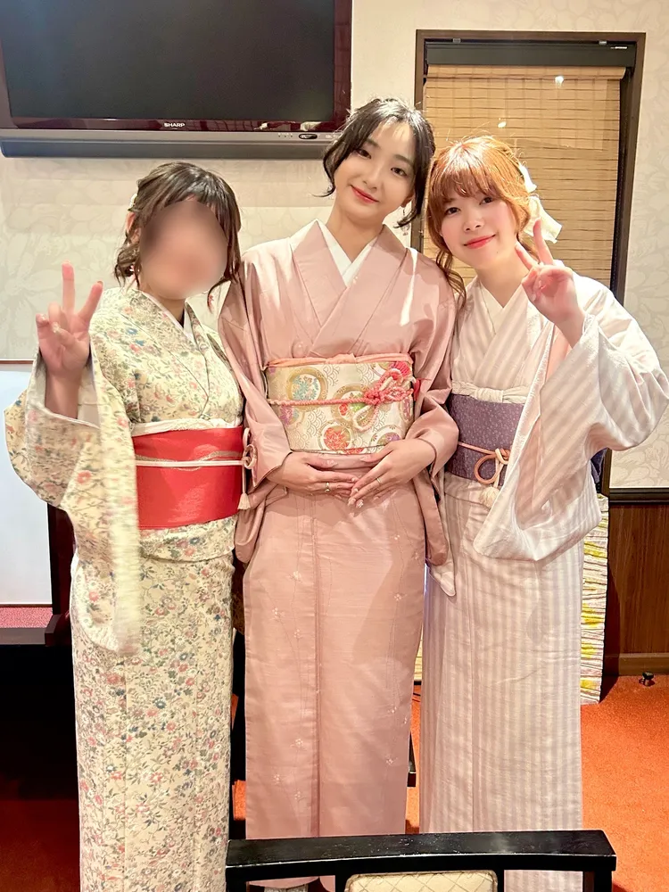 Three women in kimono of different patterns and colors posing together indoors; one person's face is blurred for privacy.