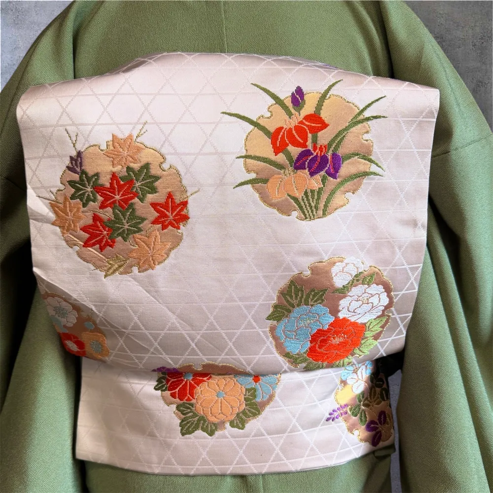 Close-up of a cream obi with maple leaf and iris embroidery in orange, green, and purple.