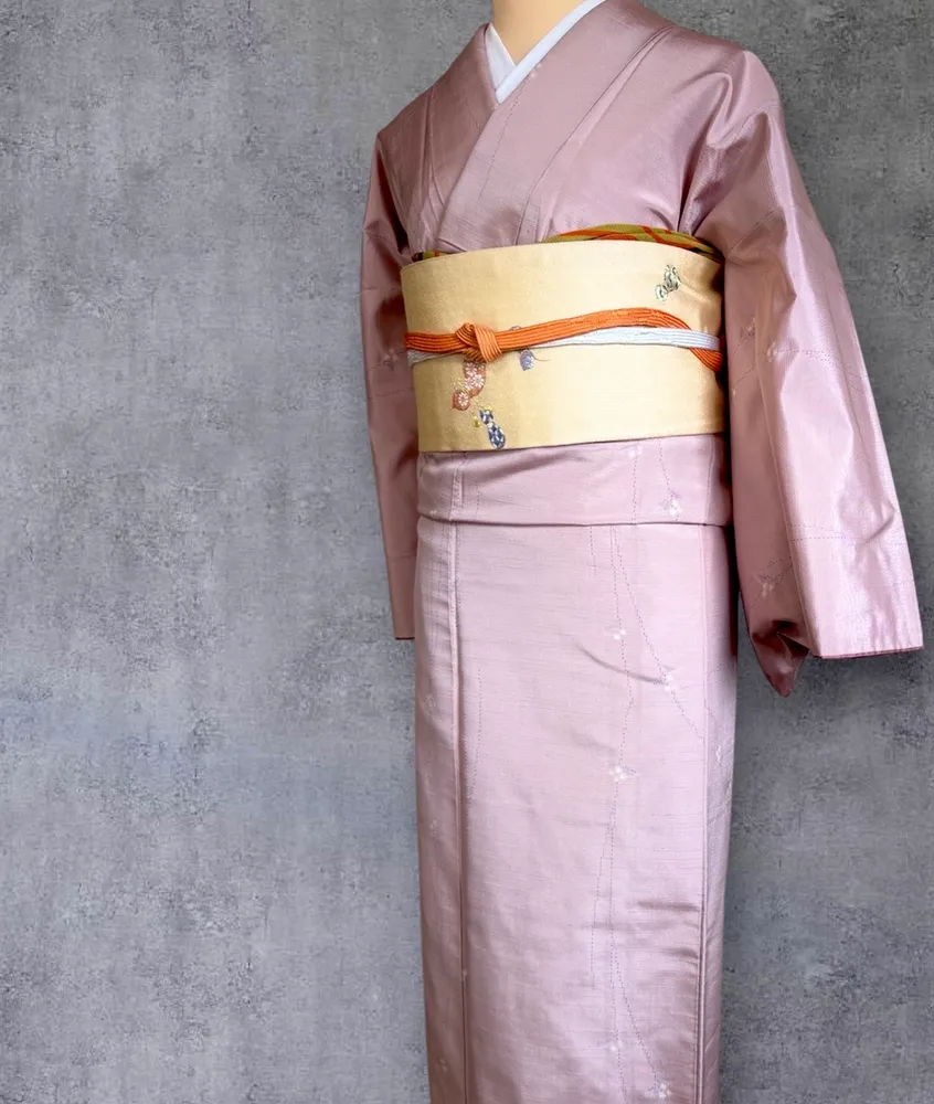 A dusty pink kimono with a pale floral pattern on a mannequin, tied with a gold obi.