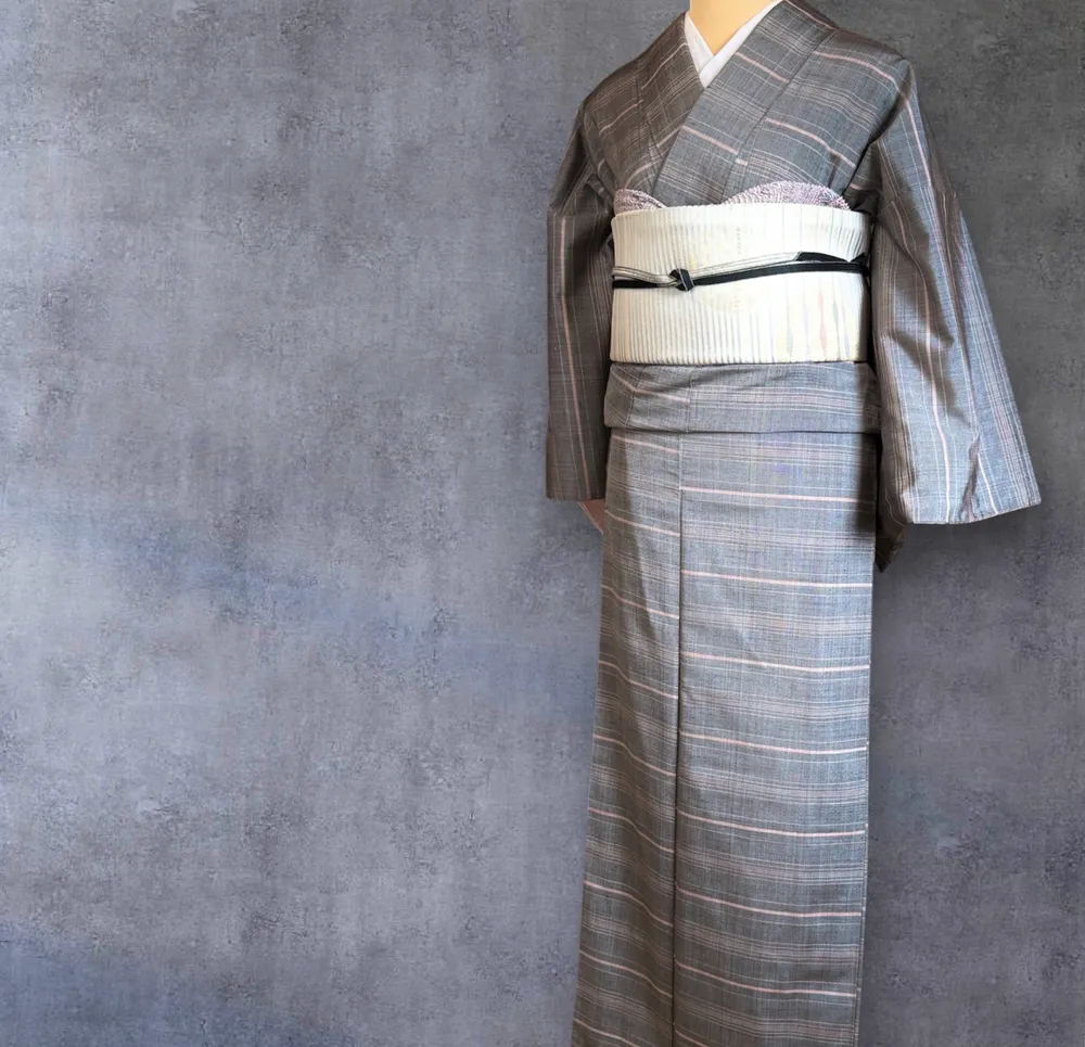 A grey kimono with fine pink stripes on a mannequin, tied with an ivory striped obi.