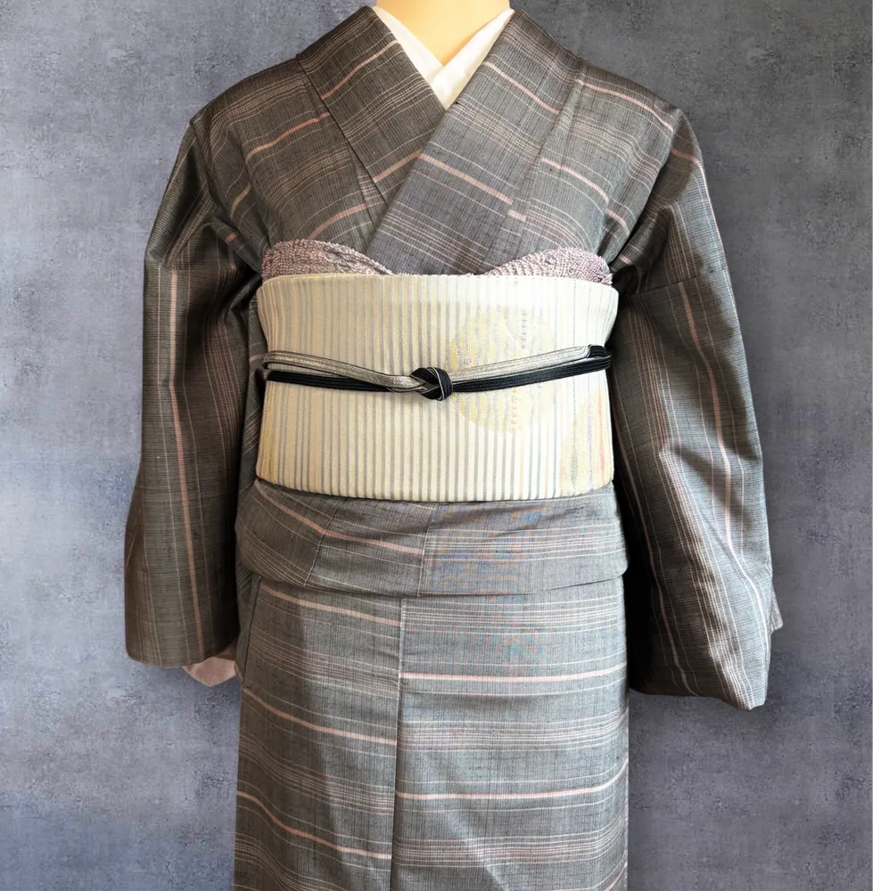 Close-up of an ivory striped obi tied with a black cord, over a grey pink-striped kimono.
