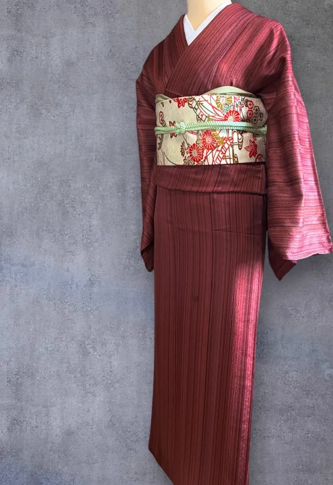 Back view of a burgundy striped kimono, showing a cream obi with a detailed red and gold chrysanthemum pattern.