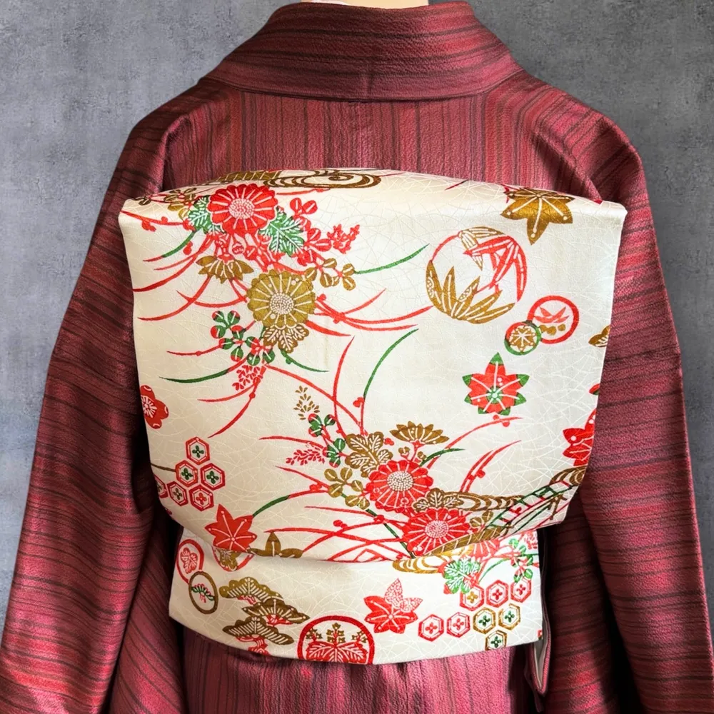 Close-up of a cream obi with a red and gold floral and geometric pattern, tied with a sage green cord.