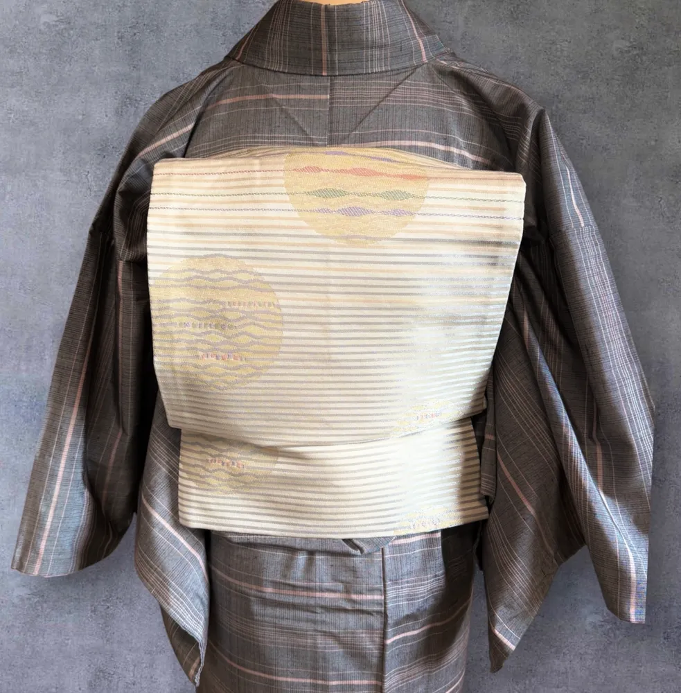 Back view of a grey plaid kimono, showing a cream obi with pale yellow circular motifs.